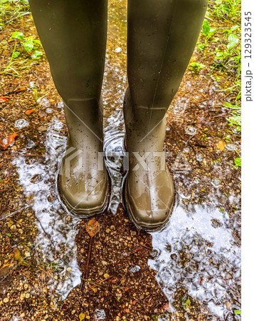 Person wearing rubber boots in shallow puddle, raindrops and mud on forest path. Rainy weather and waterproof footwear concept. High quality photo Person wearing rubber boots in shallow puddle, raindrops and mud on forest path. Rainy weather and waterproof footwear concept. High quality photo 129323545