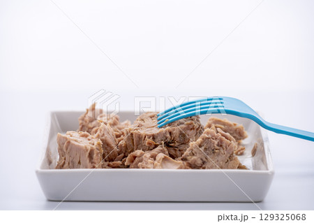 Canned tuna in brine, still in pieces with a blue plastic fork on white square plate Canned tuna in brine, still in pieces with a blue plastic fork on white square plate 129325068