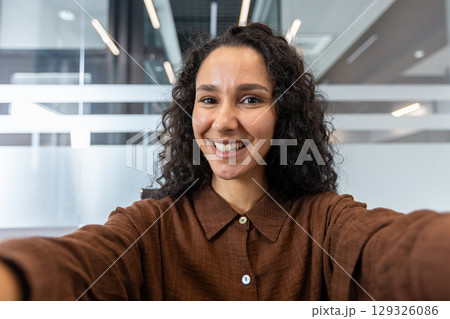 Confident woman smiles warmly at the camera in a contemporary office setting, radiating positivity. The surrounding glass partitions emphasize the professional yet approachable atmosphere. Confident woman smiles warmly at the camera in a contemporary office setting, radiating positivity. The surrounding glass partitions emphasize the professional yet approachable atmosphere. 129326086