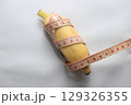 A short yellow banana wrapped with a measuring tape, placed on a clean white background. This image highlights both the length and circumference of the fruit. 129326355