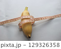 A short yellow banana wrapped with a measuring tape, placed on a clean white background. This image highlights both the length and circumference of the fruit. 129326358