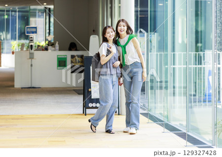友達と大学構内を歩く女子大生 129327428
