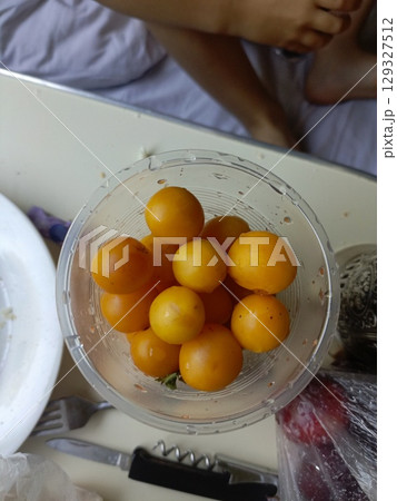 Yellow cherry tomatoes in a clear bowl in a high-angle, casual style representing fresh ingredients and healthy snacking 129327512
