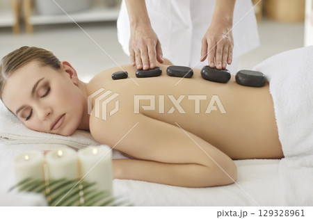 Woman enjoying back body treatment with hot stones getting massage therapy in spa salon 129328961