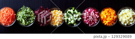 A row of bowls containing colorful, chopped vegetables is placed on a dark surface. Concept of diversity in fresh ingredients. For healthy eating inspiration. 129329089