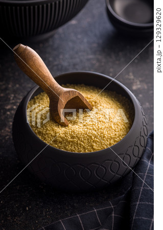 Raw couscous in bowl on black table. 129329620