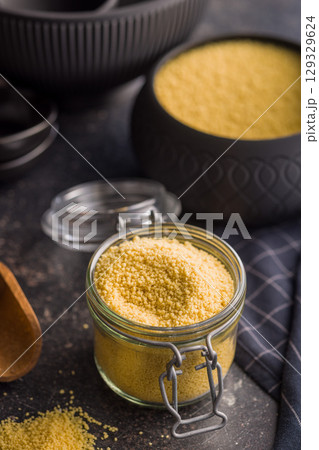 Raw couscous in jar on black table. 129329624