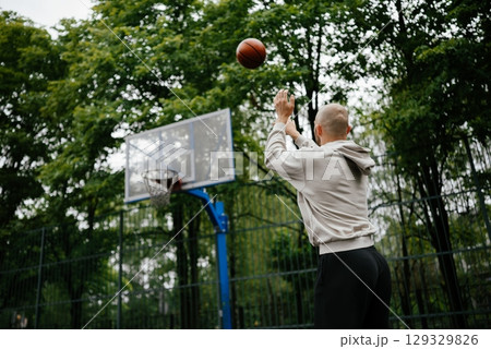 Outdoor Basketball Shot by Man in Hoodie on Court 129329826