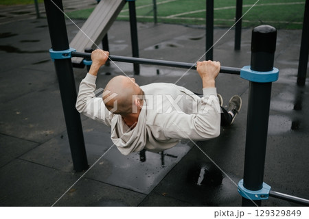 Man Performing Inverted Row on Outdoor Gym Equipment 129329849