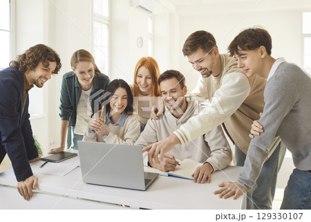 Cheerful young colleagues or students looking at laptop, discussing project and sharing ideas. 129330107