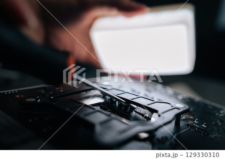 Close-up cropped shot of repairman using screwdriver to remove old thermal paste from CPU socket of motherboard, preparing for installation of new processor. Concept of desktop PC maintenance, service 129330310