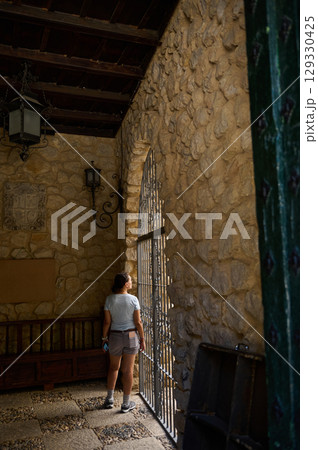 Woman Standing by Stone Architectural Window Viewing Sunlit Exterior 129330425