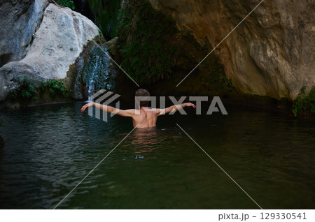 Man Bathing in a Serene Rock Pool Surrounded by Natural Greenery Man Bathing in a Serene Rock Pool Surrounded by Natural Greenery 129330541
