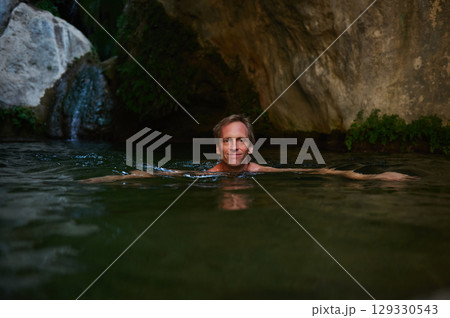 Relaxed Man Swimming in a Serene Natural Spring Surrounded by Rocks Relaxed Man Swimming in a Serene Natural Spring Surrounded by Rocks 129330543
