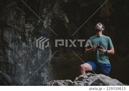 Man in Green Shirt Holding a Cup in a Dimly Lit Cave Surrounded by Rocky Walls Man in Green Shirt Holding a Cup in a Dimly Lit Cave Surrounded by Rocky Walls 129330613