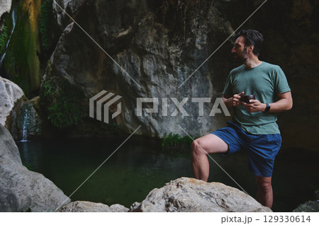 Man Relaxing Near a Scenic Rocky Waterfall in a Tranquil Forest Man Relaxing Near a Scenic Rocky Waterfall in a Tranquil Forest 129330614