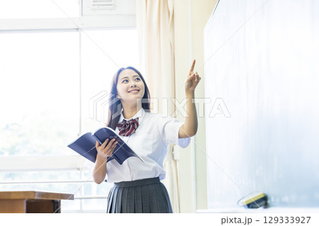 黒板の前で発表する女子高生 129333927
