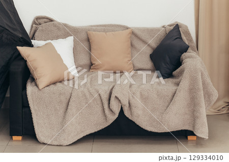 A cozy sofa with colored pillows and a blanket against a light wall. Living room interior design idea A cozy sofa with colored pillows and a blanket against a light wall. Living room interior design idea 129334010