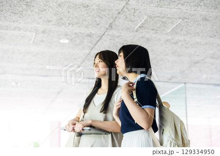 　校内で笑顔で会話するリュックの女子学生二人 129334950