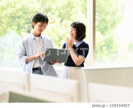 窓際で会話する大学生男女とノートPC 窓際で会話する大学生男女とノートPC 129334957