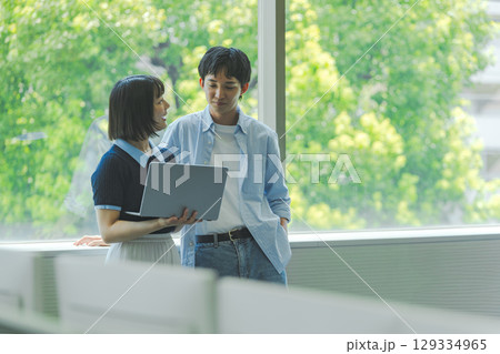 窓際で会話する大学生男女とノートPC 窓際で会話する大学生男女とノートPC 129334965