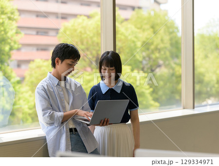 　窓際で会話する大学生男女とノートPC 129334971