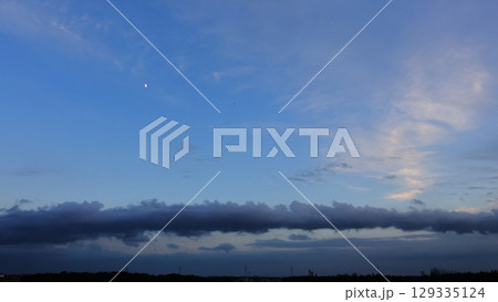 気象　層積雲　ロール雲。夏の夕暮れ、上弦の月の下に空を跨ぐ水平の雲 129335124