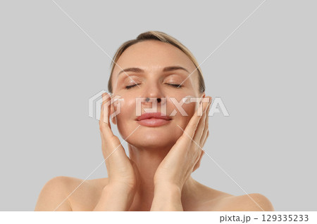 Woman gently massaging cream on her face with closed eyes Woman gently massaging cream on her face with closed eyes 129335233