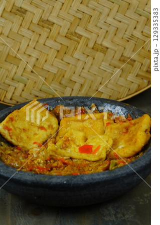 Tahu tempe penyet or Indonesian fried tofu and tempeh served on a dark stone mortar with a vibrant red chili paste known as sambal. Tahu tempe penyet or Indonesian fried tofu and tempeh served on a dark stone mortar with a vibrant red chili paste known as sambal. 129335383