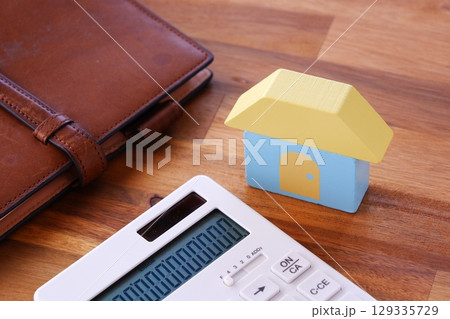 家と電卓で、あこがれのマイホームを購入するために資金計画を立てているイメージ 129335729