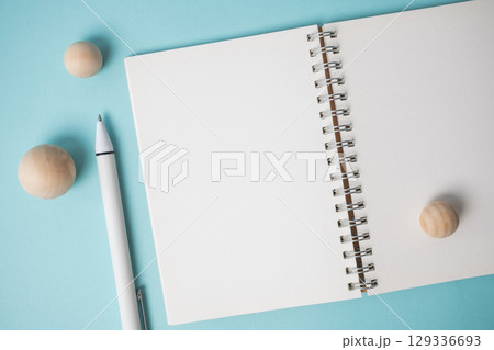Workspace with empty notebook, pen and wooden ball on blue background. Workspace with empty notebook, pen and wooden ball on blue background. 129336693