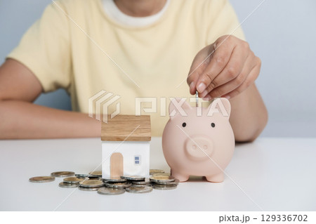 Woman hand putting money coin into pink piggy bank for for savings money. 129336702