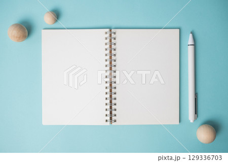 Workspace with empty notebook, pen and wooden ball on blue background. Workspace with empty notebook, pen and wooden ball on blue background. 129336703