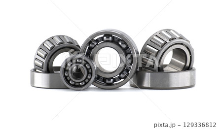 Diverse collection of mechanical ball and roller bearings sits on a clean white surface. 129336812