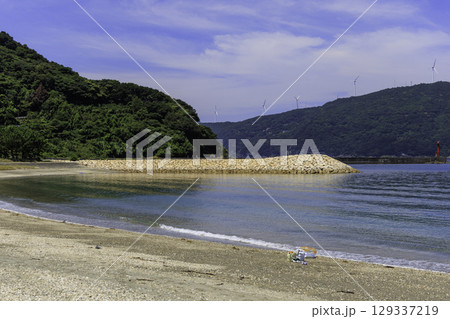 砂浜から望むムーンビーチ井野浦と防波堤、遠くに見える風車の夏景色 砂浜から望むムーンビーチ井野浦と防波堤、遠くに見える風車の夏景色 129337219