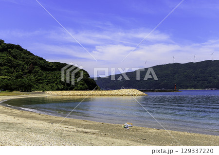 砂浜から望むムーンビーチ井野浦と防波堤、遠くに見える風車の夏景色 129337220
