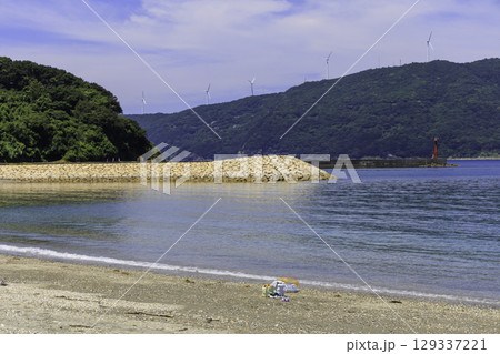 砂浜から望むムーンビーチ井野浦と防波堤、遠くに見える風車の夏景色 129337221