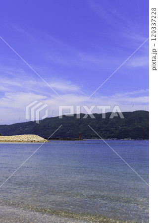 砂浜から望むムーンビーチ井野浦と防波堤、遠くに見える風車の夏景色 129337228