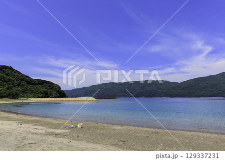 砂浜から望むムーンビーチ井野浦と防波堤、遠くに見える風車の夏景色 129337231
