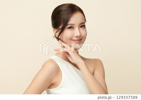 A beautiful young Asian woman with clean, fresh skin against a beige background. Skincare, facial treatment, cosmetology, beauty, and spa. An elegant portrait of an Asian woman. 129337389