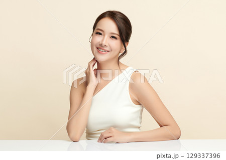 A beautiful young Asian woman with clean, fresh skin against a beige background. Skincare, facial treatment, cosmetology, beauty, and spa. An elegant portrait of an Asian woman. A beautiful young Asian woman with clean, fresh skin against a beige background. Skincare, facial treatment, cosmetology, beauty, and spa. An elegant portrait of an Asian woman. 129337396