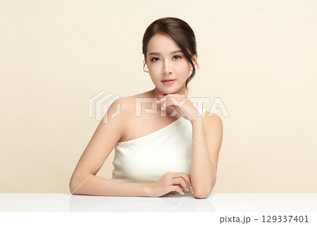 A beautiful young Asian woman with clean, fresh skin against a beige background. Skincare, facial treatment, cosmetology, beauty, and spa. An elegant portrait of an Asian woman. A beautiful young Asian woman with clean, fresh skin against a beige background. Skincare, facial treatment, cosmetology, beauty, and spa. An elegant portrait of an Asian woman. 129337401