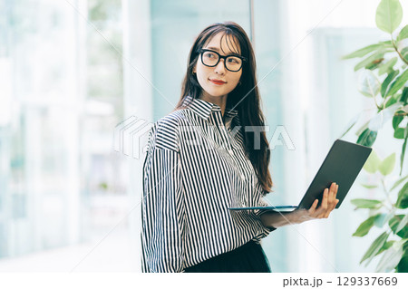 オフィスの窓際でノートパソコンを持つミドルのビジネスウーマン 129337669