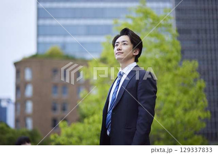 ビルを背景に遠くを見つめるスーツを着た日本人ビジネスマンの男性 129337833