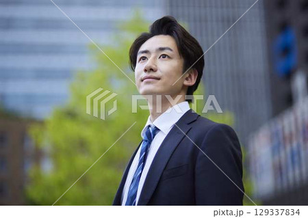 ビルを背景に遠くを見つめるスーツを着た日本人ビジネスマンの男性 129337834