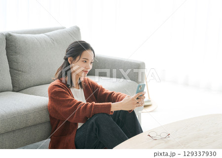 リビングでスマホを見る若い女性 129337930