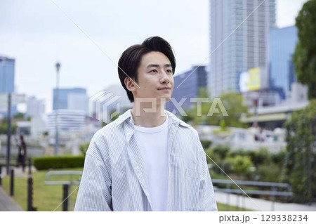 ビルを背景に公園を歩く20代日本人男性 ビルを背景に公園を歩く20代日本人男性 129338234