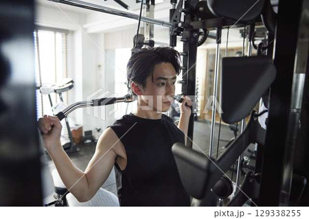 男性がフィットネスジムのマシンで胸と肩を鍛える筋力トレーニング 129338255