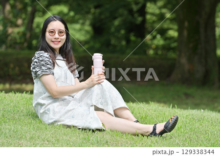 芝生に座って水筒の水を飲み休憩する若い女性 129338344