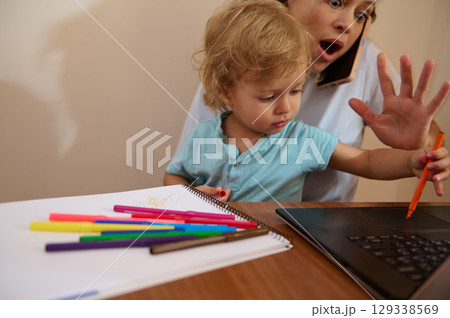 Mother Balancing Remote Work While Engaging with Curious Toddler at Home 129338569